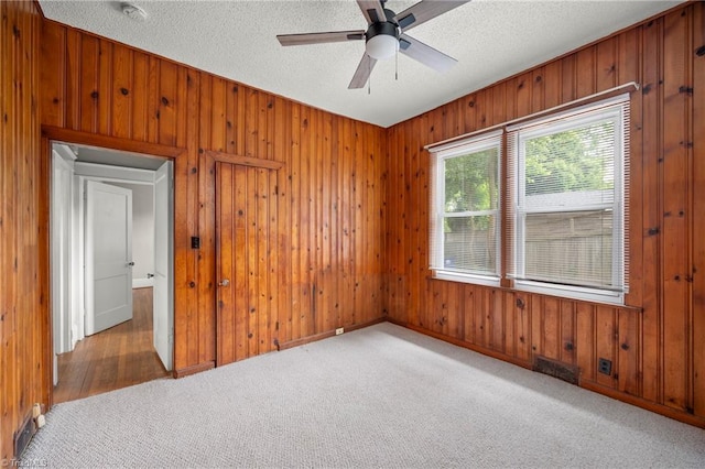 carpeted empty room with wood walls, ceiling fan, a textured ceiling, baseboards, and a smoke detector