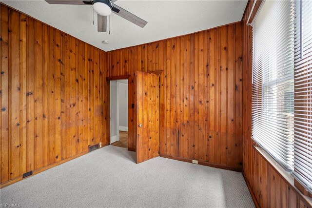 carpeted empty room featuring wood walls and a ceiling fan