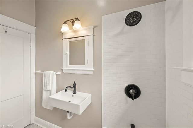 full bathroom with tiled shower, a sink, and baseboards