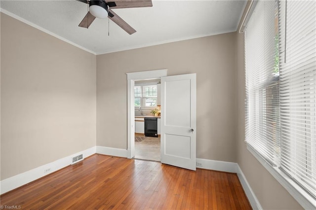spare room featuring wood-type flooring, baseboards, ceiling fan, and crown molding