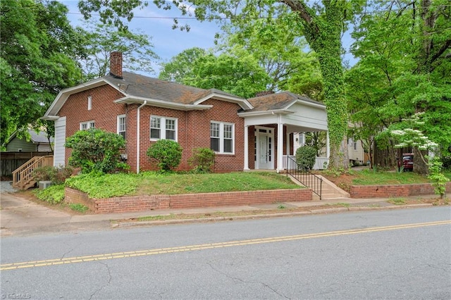 bungalow featuring a chimney, brick siding, and covered porch