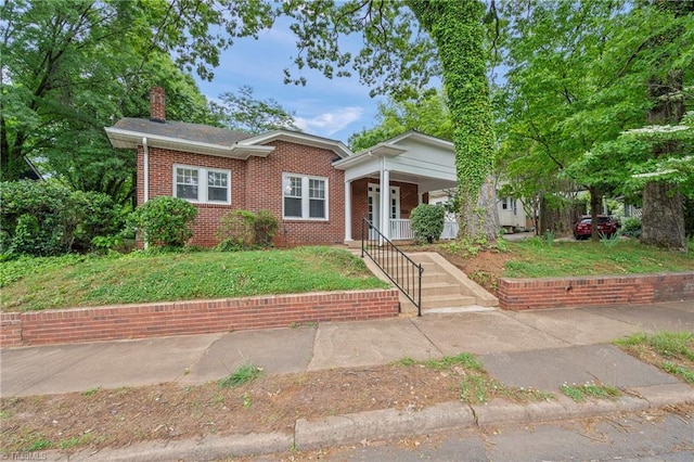 bungalow with a chimney, brick siding, covered porch, and a front yard