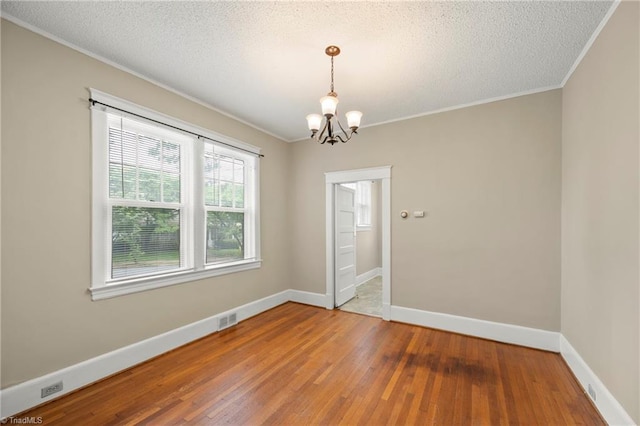 unfurnished room featuring wood-type flooring, a chandelier, crown molding, baseboards, and a textured ceiling
