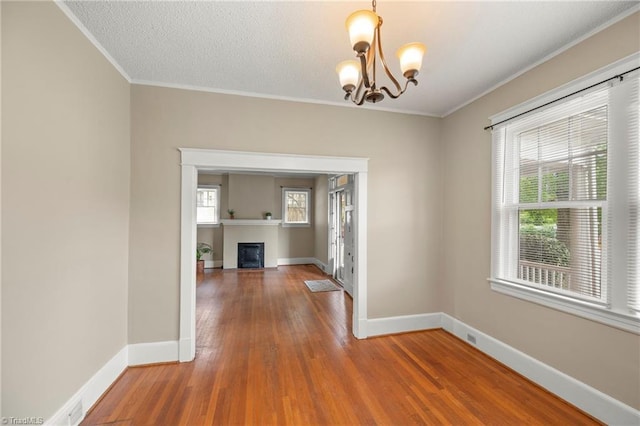 spare room featuring a chandelier, ornamental molding, wood finished floors, baseboards, and a fireplace with flush hearth