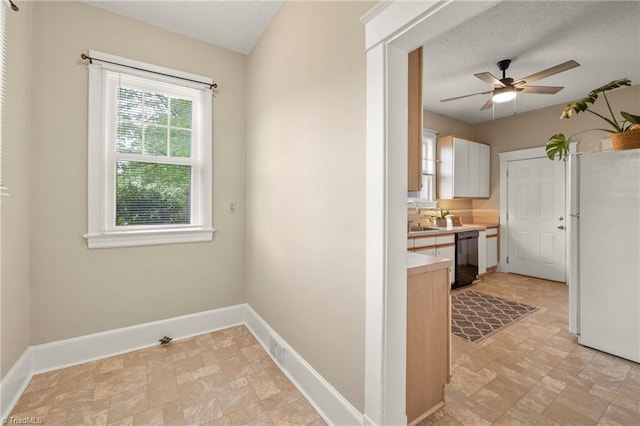 kitchen with freestanding refrigerator, black dishwasher, stone finish floors, a ceiling fan, and a textured ceiling