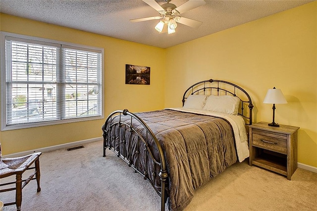 bedroom with ceiling fan, light colored carpet, and a textured ceiling