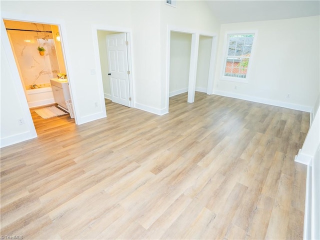 unfurnished bedroom with ensuite bathroom, a closet, light wood-type flooring, and vaulted ceiling