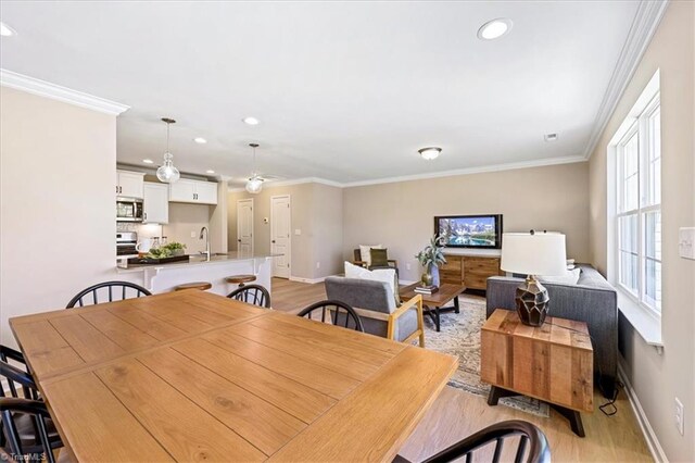 dining room featuring baseboards, light wood-type flooring, ornamental molding, and recessed lighting