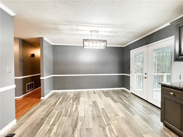 unfurnished dining area with ornamental molding, light wood-type flooring, a textured ceiling, and french doors