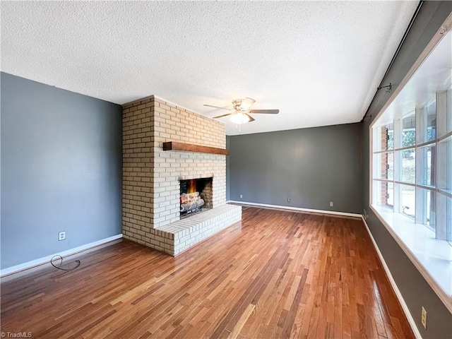 unfurnished living room with ceiling fan, a textured ceiling, hardwood / wood-style floors, and a fireplace