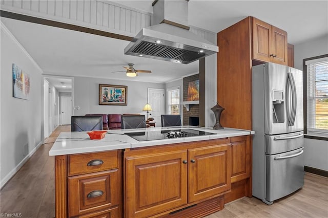 kitchen featuring brown cabinets, wall chimney range hood, black electric stovetop, and stainless steel refrigerator with ice dispenser