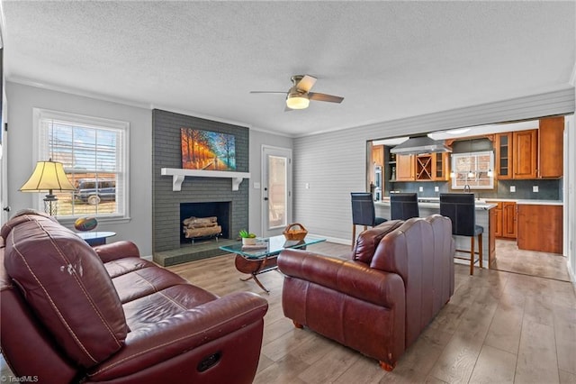 living area with a textured ceiling, ornamental molding, light wood-type flooring, and a brick fireplace