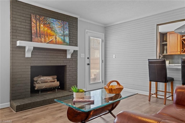 living room with a textured ceiling, a fireplace, light wood-style floors, baseboards, and crown molding