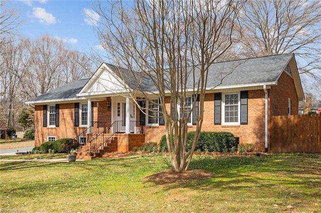 single story home featuring a shingled roof, a front yard, fence, and brick siding