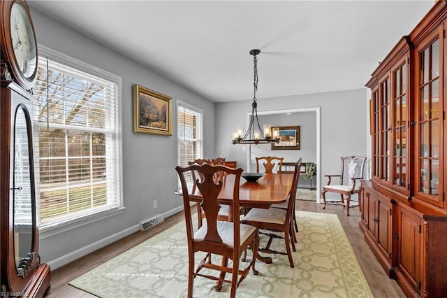 dining space with light wood-type flooring, baseboards, visible vents, and a chandelier