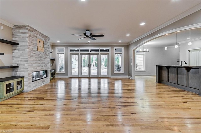 unfurnished living room with ornamental molding, ceiling fan, a fireplace, and light wood-type flooring