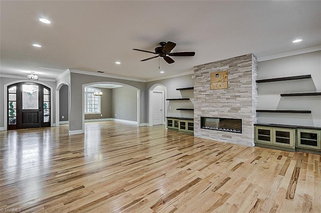 unfurnished living room featuring ceiling fan, ornamental molding, light wood-type flooring, and a fireplace