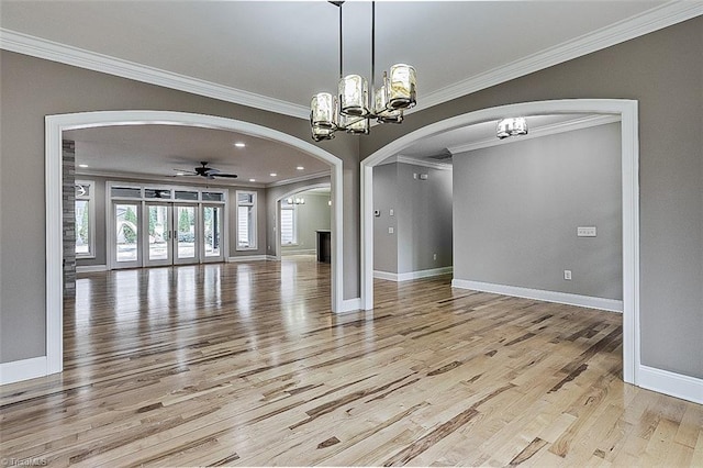 unfurnished dining area with ornamental molding, ceiling fan with notable chandelier, and light wood-type flooring