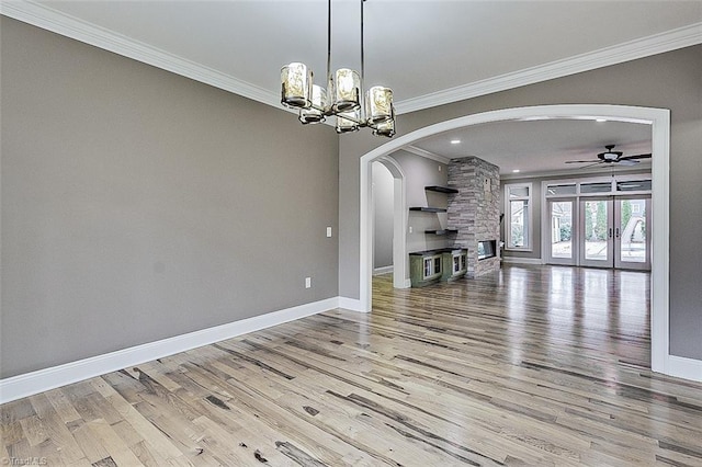 unfurnished living room with crown molding, ceiling fan with notable chandelier, and light wood-type flooring