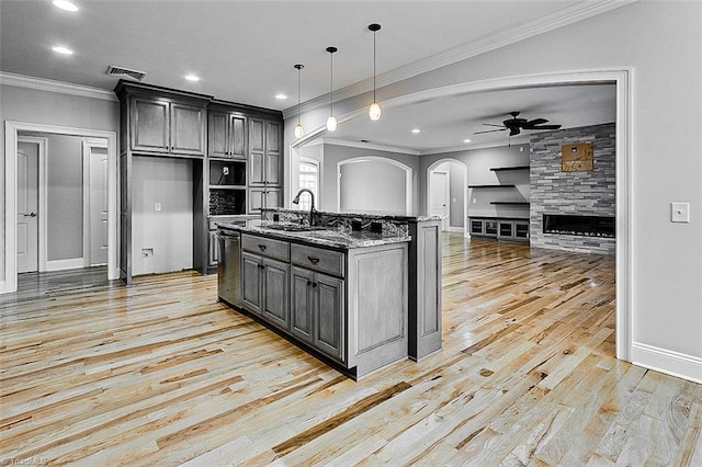 kitchen with decorative light fixtures, stainless steel dishwasher, an island with sink, stone counters, and light hardwood / wood-style floors