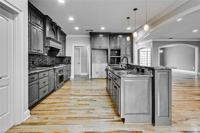 kitchen featuring pendant lighting, sink, a kitchen island with sink, decorative backsplash, and dark stone counters