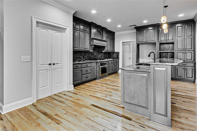 kitchen with sink, hanging light fixtures, ornamental molding, a kitchen island with sink, and light stone countertops