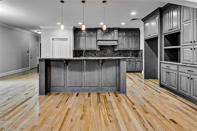 kitchen with hanging light fixtures, an island with sink, gray cabinetry, and decorative backsplash