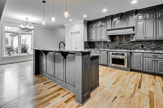 kitchen featuring a breakfast bar area, oven, hanging light fixtures, and a center island with sink