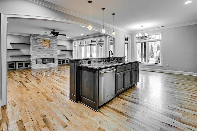 kitchen featuring stone countertops, ceiling fan with notable chandelier, decorative light fixtures, stainless steel dishwasher, and a center island with sink