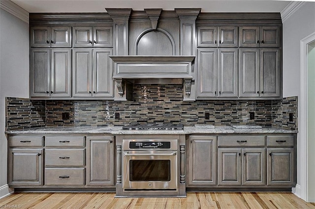 kitchen with ornamental molding, light stone countertops, light hardwood / wood-style floors, and appliances with stainless steel finishes