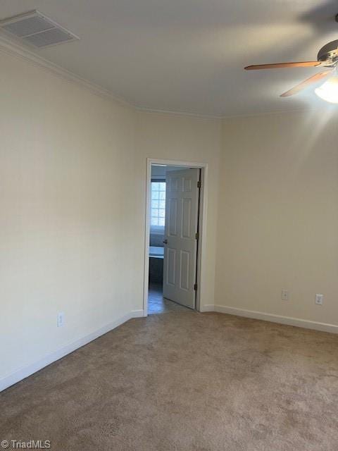 carpeted spare room featuring baseboards, ceiling fan, visible vents, and crown molding