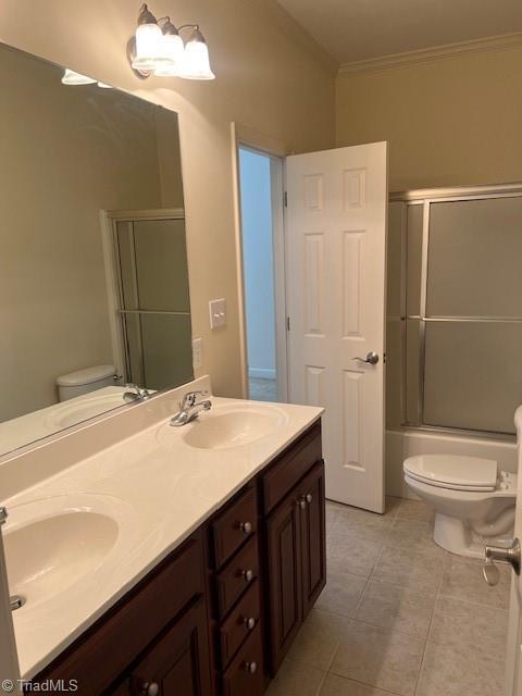 bathroom with crown molding, a sink, toilet, and bath / shower combo with glass door