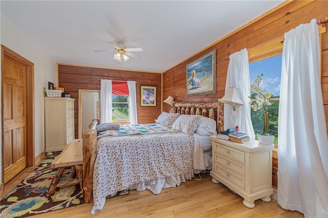 bedroom with ceiling fan, wooden walls, and light hardwood / wood-style floors