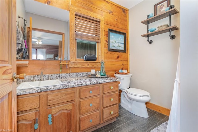 bathroom with vanity, toilet, ceiling fan, and wooden walls