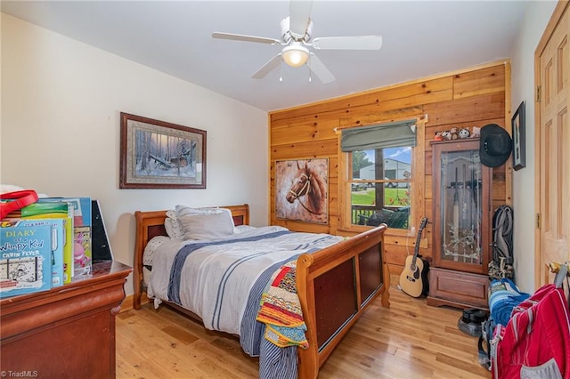 bedroom featuring ceiling fan, wood walls, and light wood-type flooring