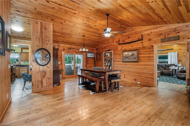 dining area with ceiling fan with notable chandelier, light hardwood / wood-style floors, lofted ceiling, and wood walls