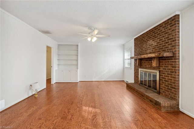 unfurnished living room with built in shelves, wood-type flooring, a textured ceiling, ceiling fan, and a fireplace