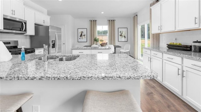 kitchen featuring a breakfast bar area, stainless steel appliances, white cabinets, dark hardwood / wood-style flooring, and light stone counters