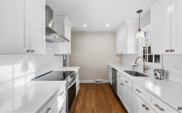 kitchen featuring sink, hanging light fixtures, wall chimney range hood, white cabinets, and appliances with stainless steel finishes