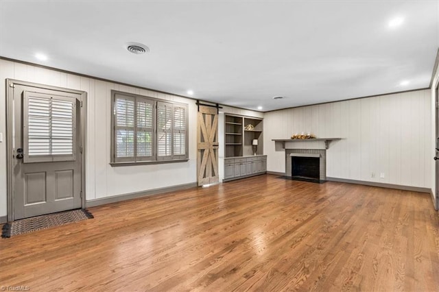 unfurnished living room featuring a barn door, crown molding, a fireplace, and light hardwood / wood-style floors