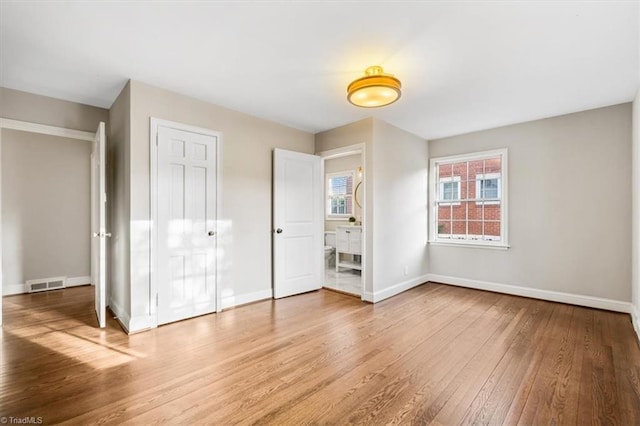 unfurnished bedroom with ensuite bath and hardwood / wood-style flooring