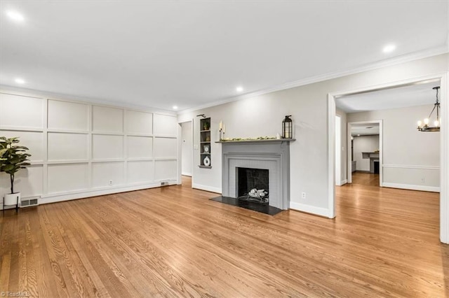 unfurnished living room with an inviting chandelier, light hardwood / wood-style floors, a brick fireplace, and crown molding