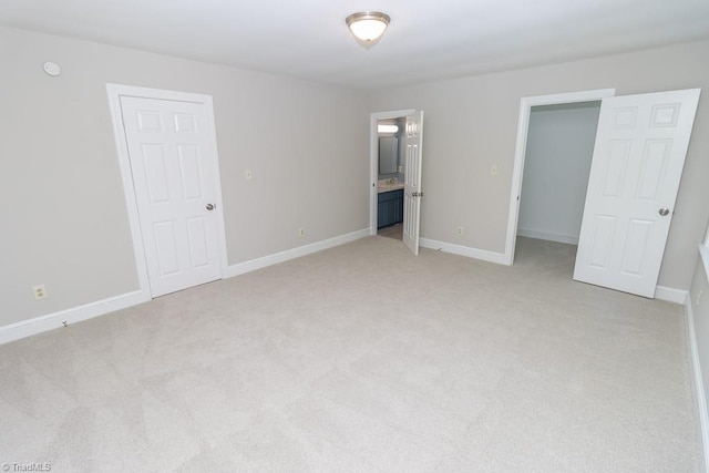 unfurnished bedroom with a walk in closet, light colored carpet, baseboards, a closet, and connected bathroom
