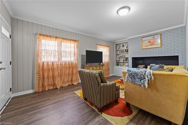 living area featuring a brick fireplace, crown molding, built in shelves, and wood finished floors