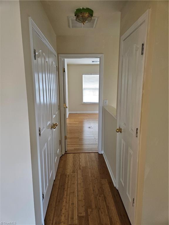 hall with baseboards, visible vents, and dark wood-style flooring