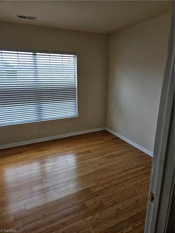 unfurnished room with wood finished floors, visible vents, and baseboards