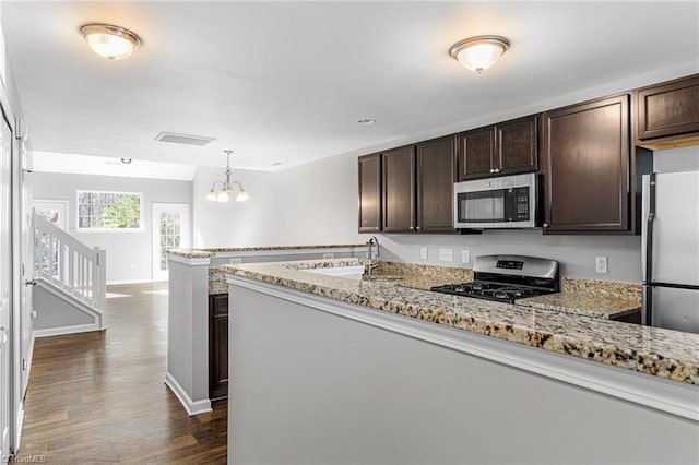 kitchen featuring hanging light fixtures, appliances with stainless steel finishes, dark brown cabinets, and light stone counters