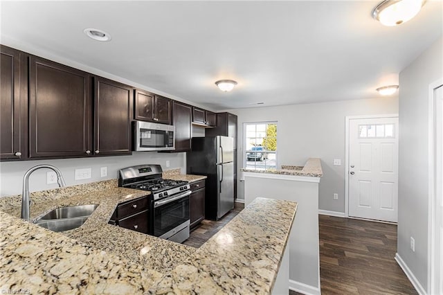 kitchen with dark wood-type flooring, dark brown cabinetry, sink, appliances with stainless steel finishes, and light stone countertops