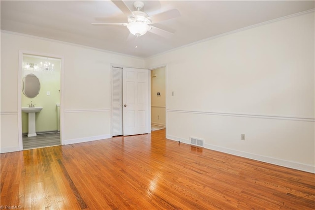 unfurnished bedroom with wood finished floors, baseboards, visible vents, ornamental molding, and connected bathroom