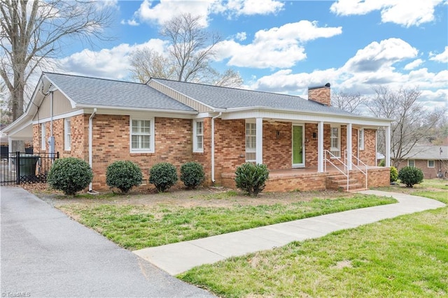 view of front facade featuring a front yard, a porch, a shingled roof, a chimney, and brick siding